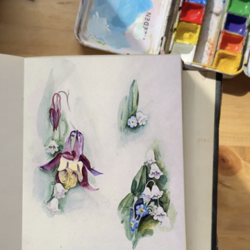 Photograph of a books open to a page with small paintings of flowers in watercolor. In the top-right corner is a small watercolor palette.